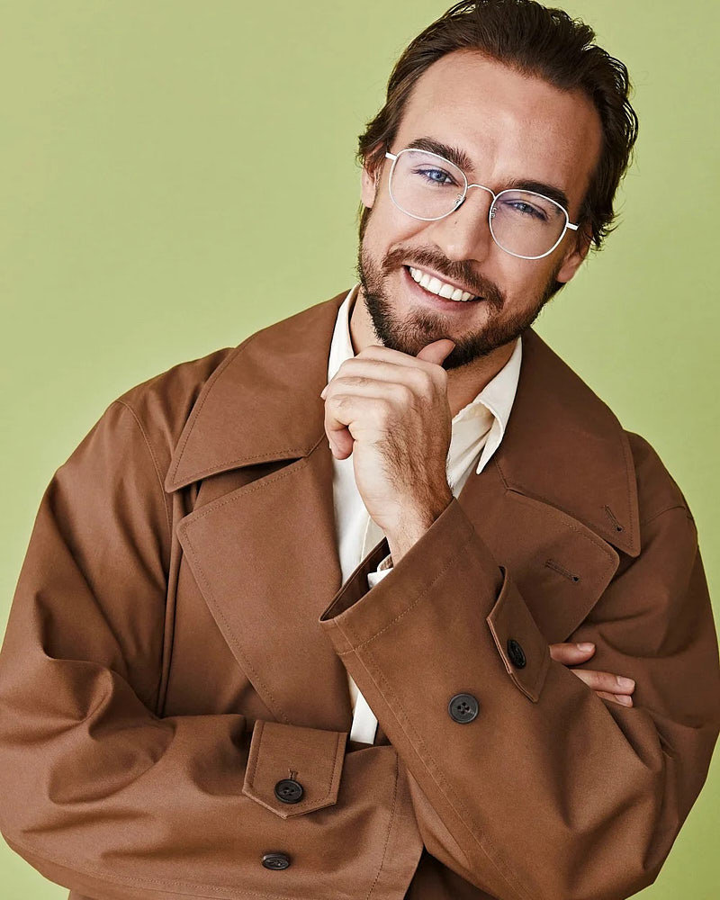 Commercial actor portrait of a man in glasses and a brown jacket on a pale green background.