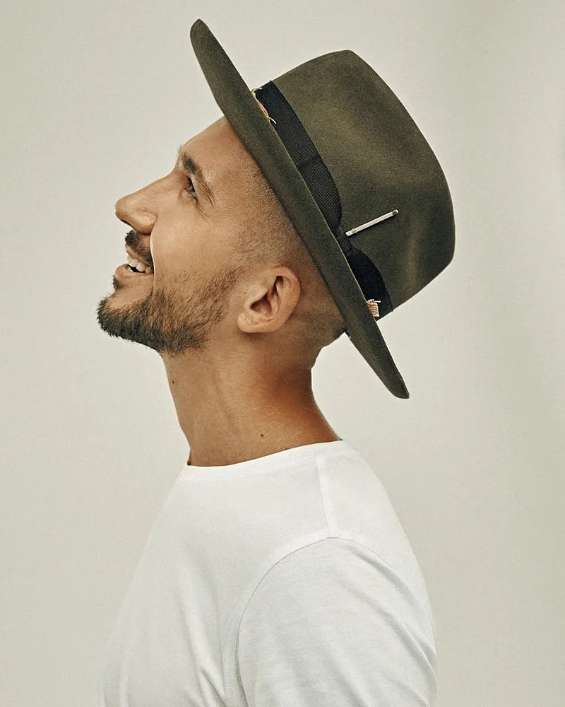 Side-profile actor portrait of a man in a hat and white shirt against a light studio background.