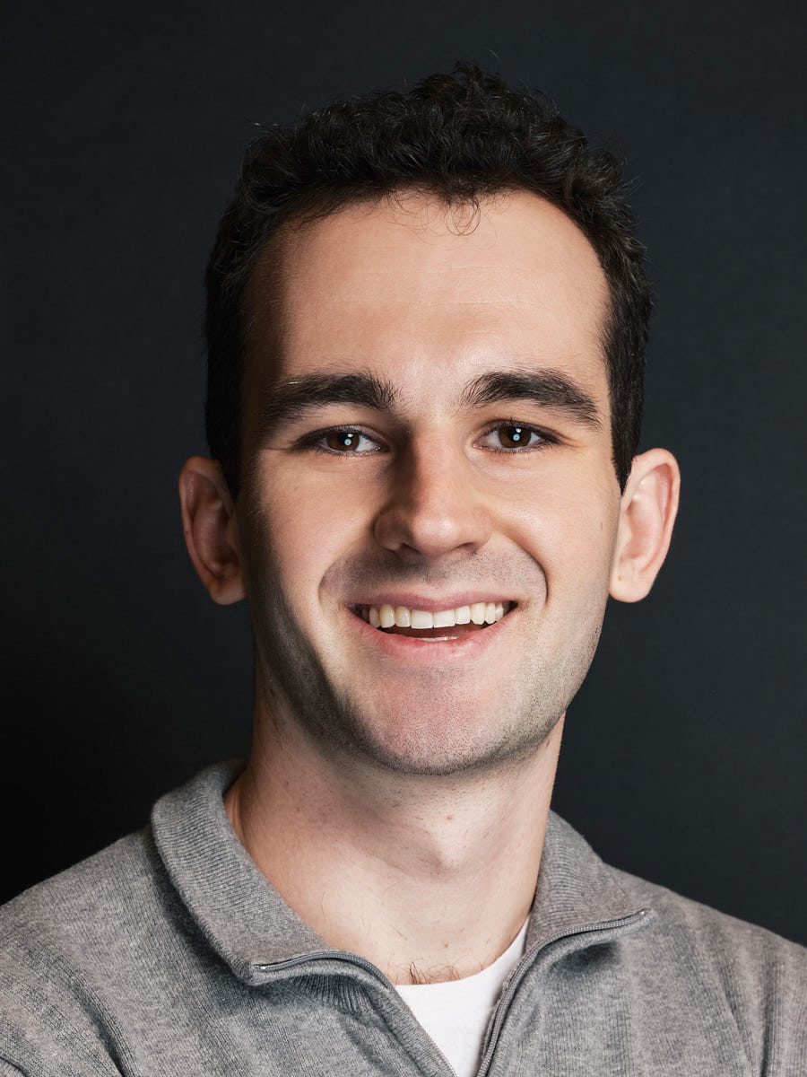Corporate headshot of a man in a gray shirt photographed against a dark background.
