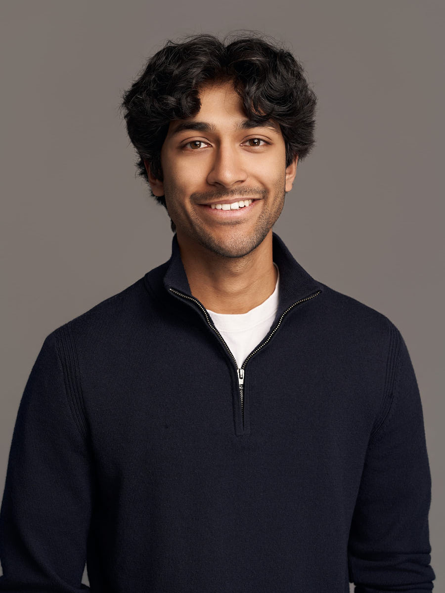 Casual executive headshot of a man in a navy sweater against a simple gray studio backdrop.