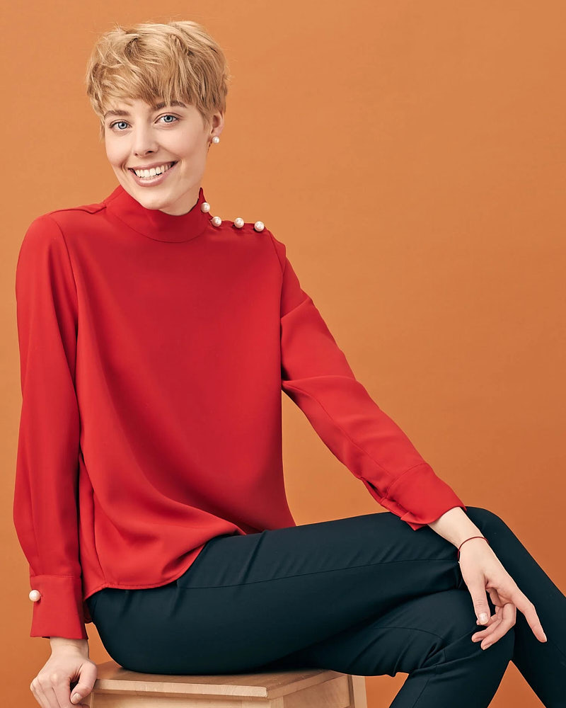 Creative executive portrait of a woman in a red sweater photographed against a warm orange studio backdrop.
