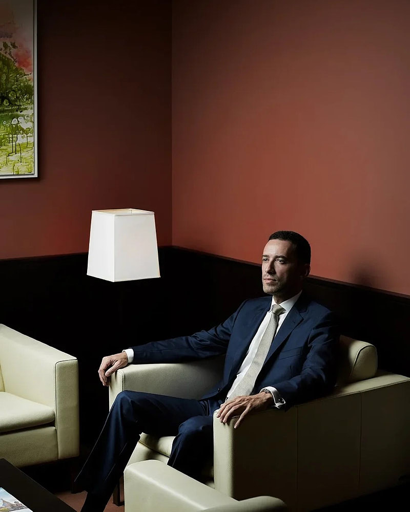 Editorial executive portrait of a suited professional seated in a modern interior.