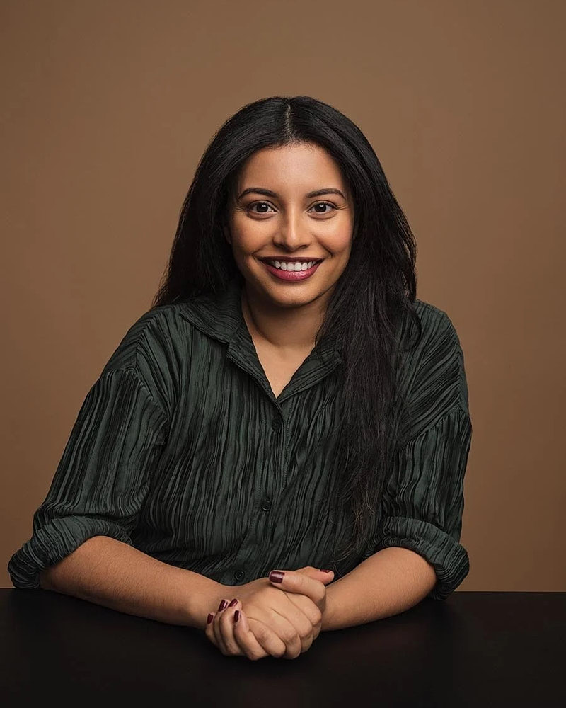 Seated executive portrait of a woman in a dark green shirt against a warm studio background.