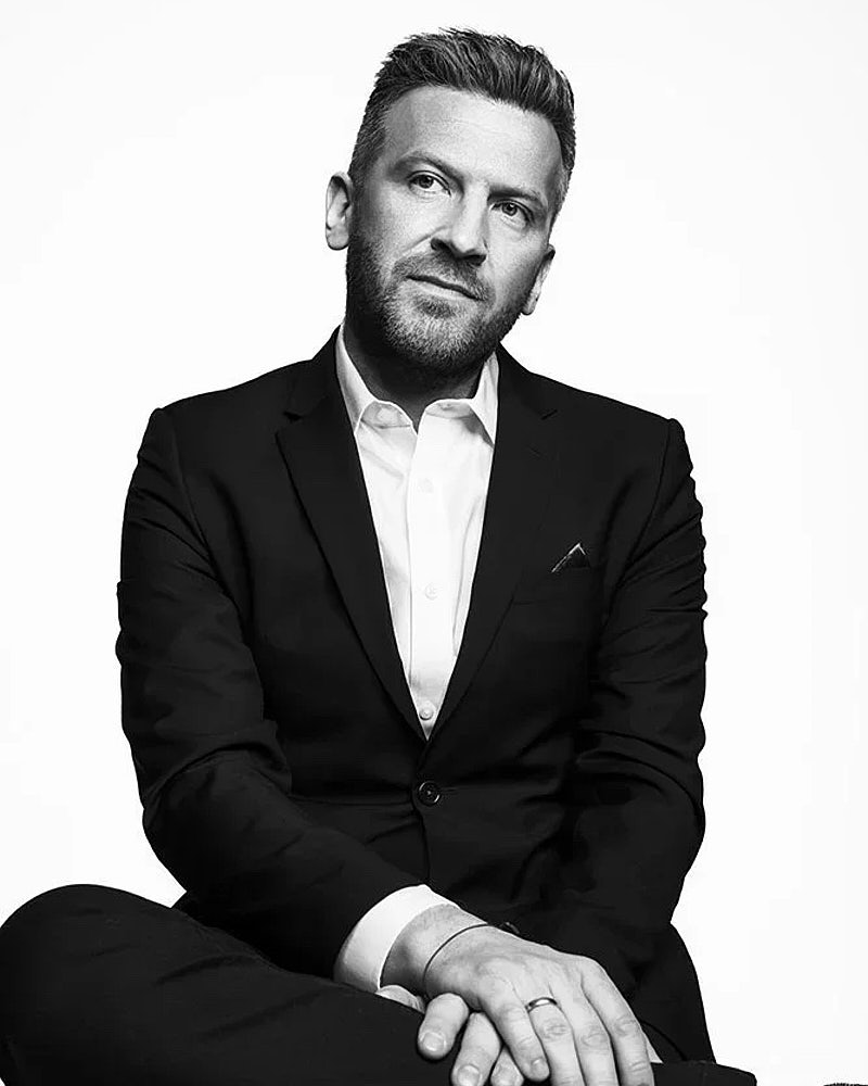 Black and white studio headshot of a man in a suit with a clean editorial look.