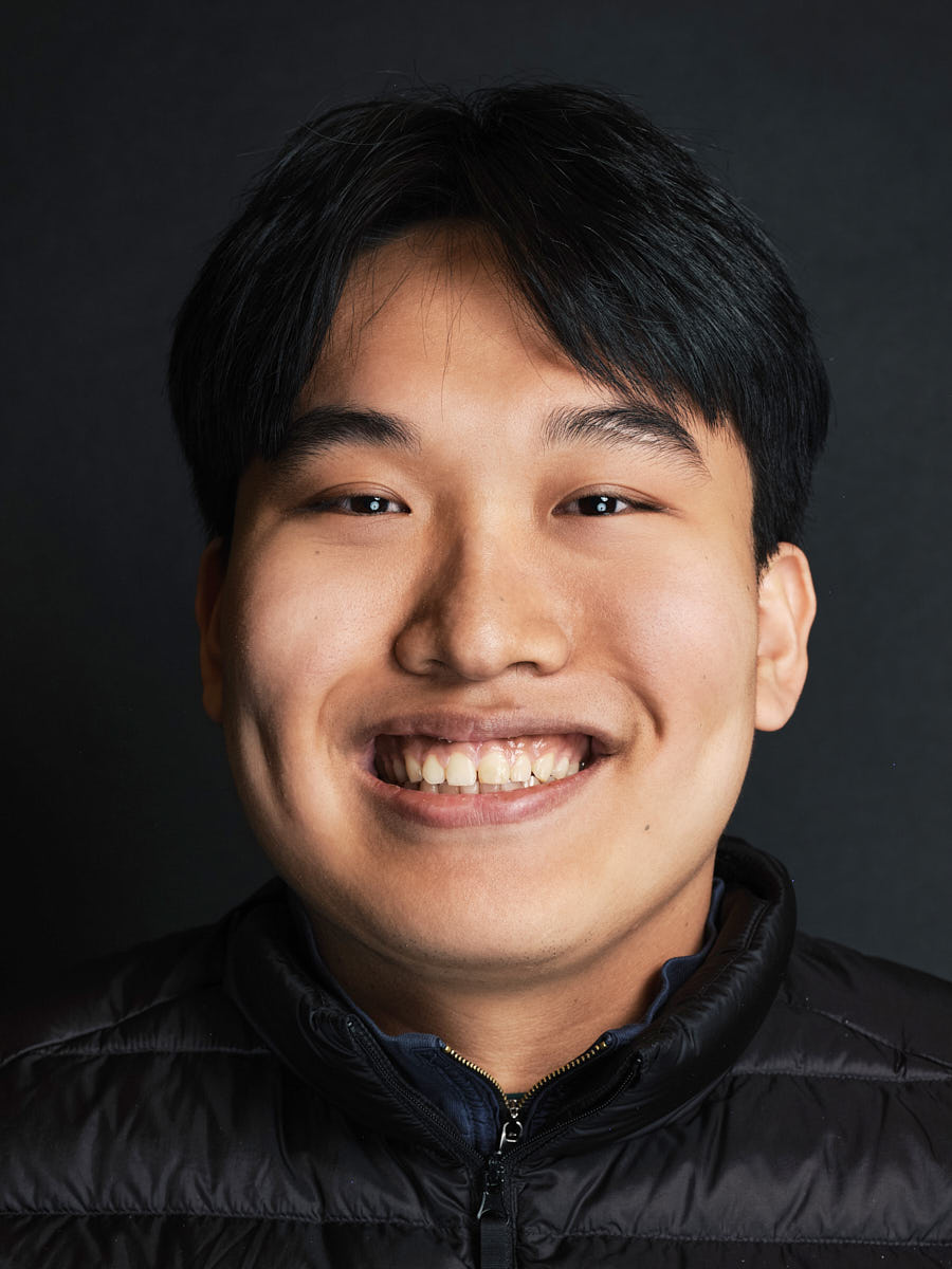 Modern smiling headshot of a young professional on a dark studio background.