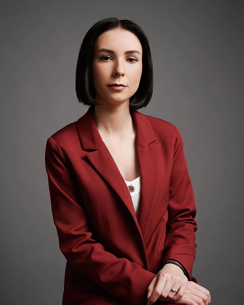 LinkedIn profile portrait of a woman in a red blazer photographed against a dark studio background.