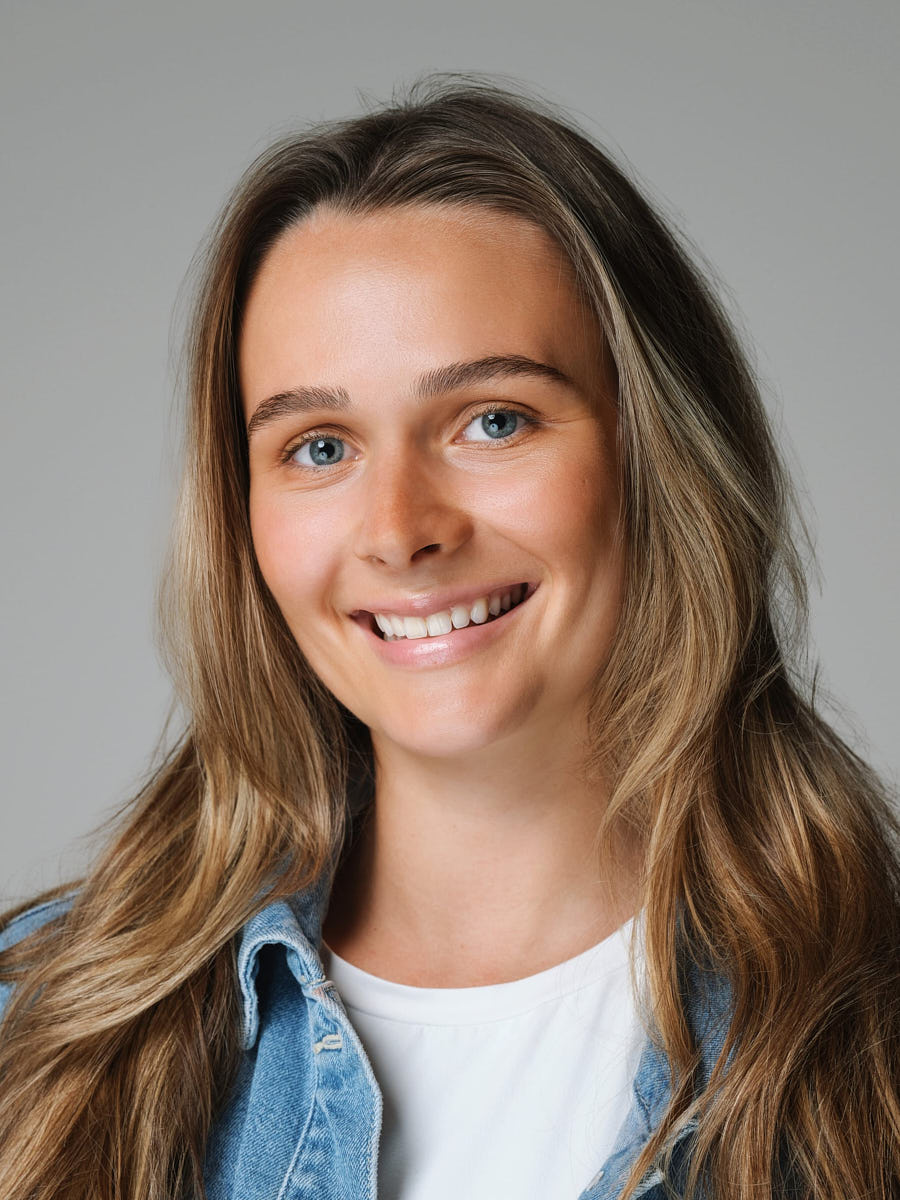 LinkedIn headshot of a woman in a denim jacket photographed on a gray studio background.