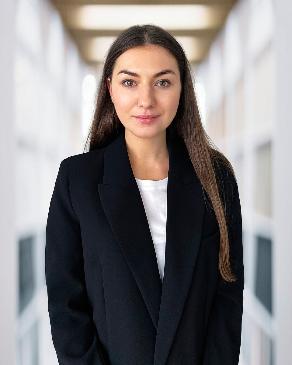Remote headshot of a blonde woman in a navy blazer photographed in a bright professional setting.