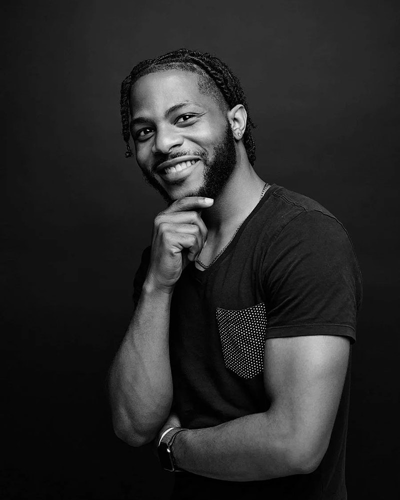 Black and white studio portrait of a man seated against a dark background.
