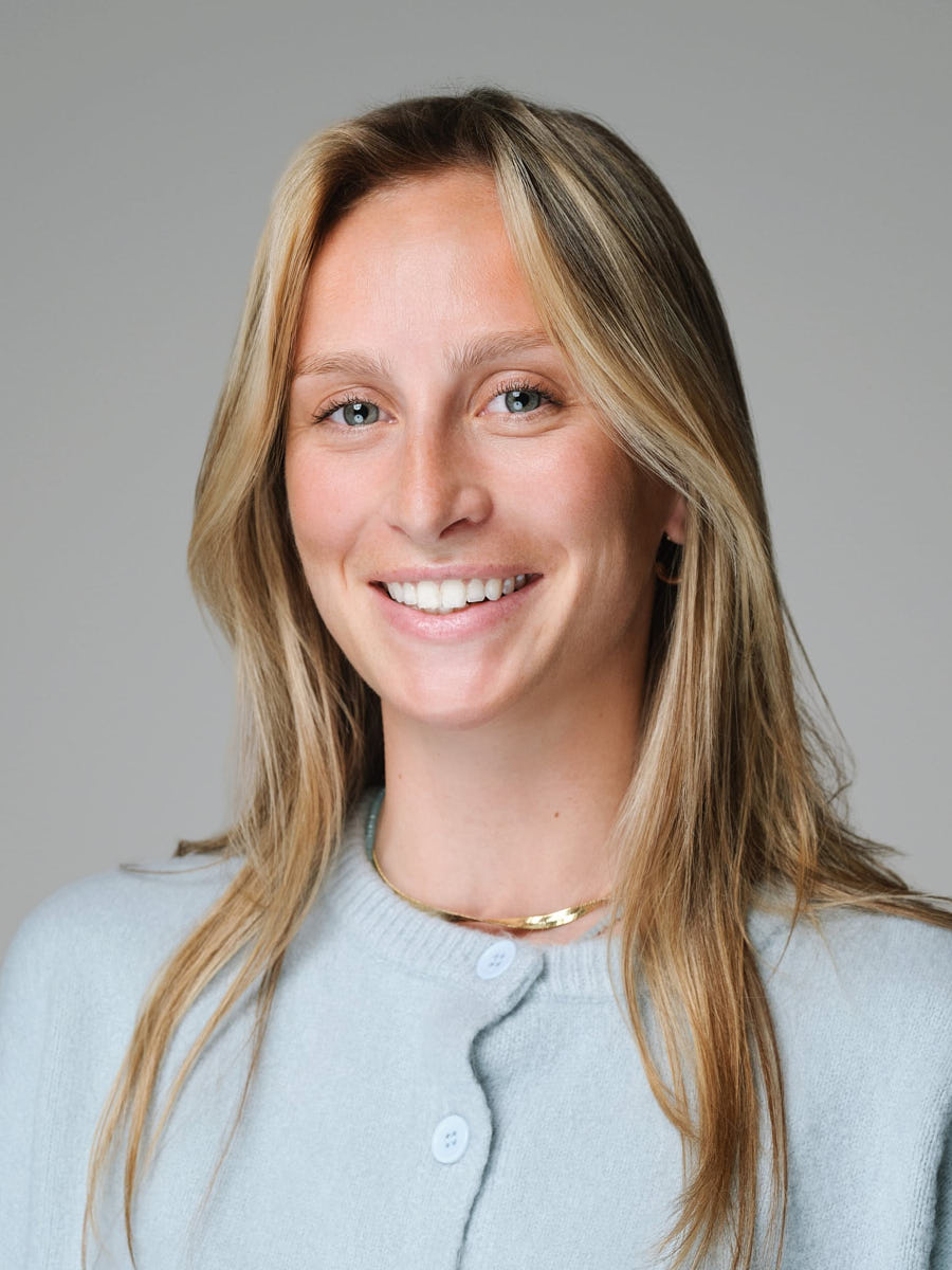 Natural studio headshot of a woman in a light cardigan photographed on a gray background.