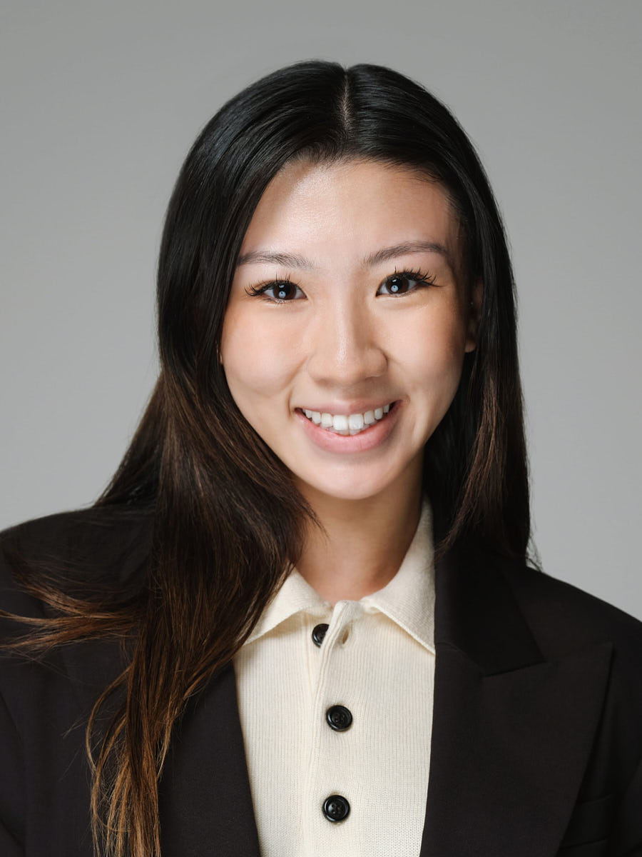 Professional studio headshot of a woman in a black blazer photographed on a gray background.