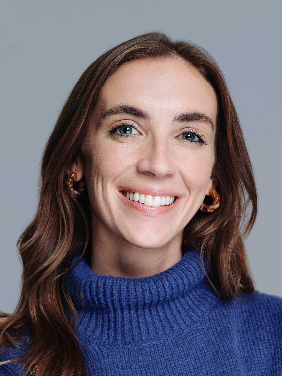 Studio headshot portfolio example of a woman in a blue sweater against a blue-gray background.