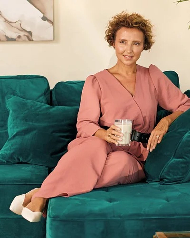 Personal branding portrait of a woman in a pink suit seated on a teal couch with a relaxed lifestyle feel.