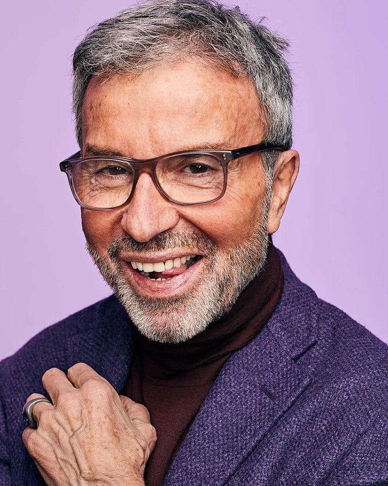 Personal branding portrait of a mature man in glasses and a purple jacket against a purple studio background.