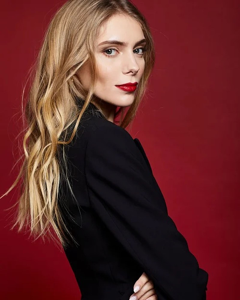 Personal branding portrait of a woman in a black blazer photographed against a deep red studio background.