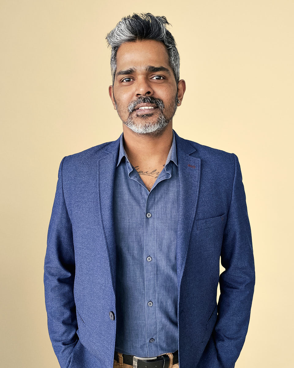 Remote headshot of a man in a blue blazer photographed against a warm yellow background.