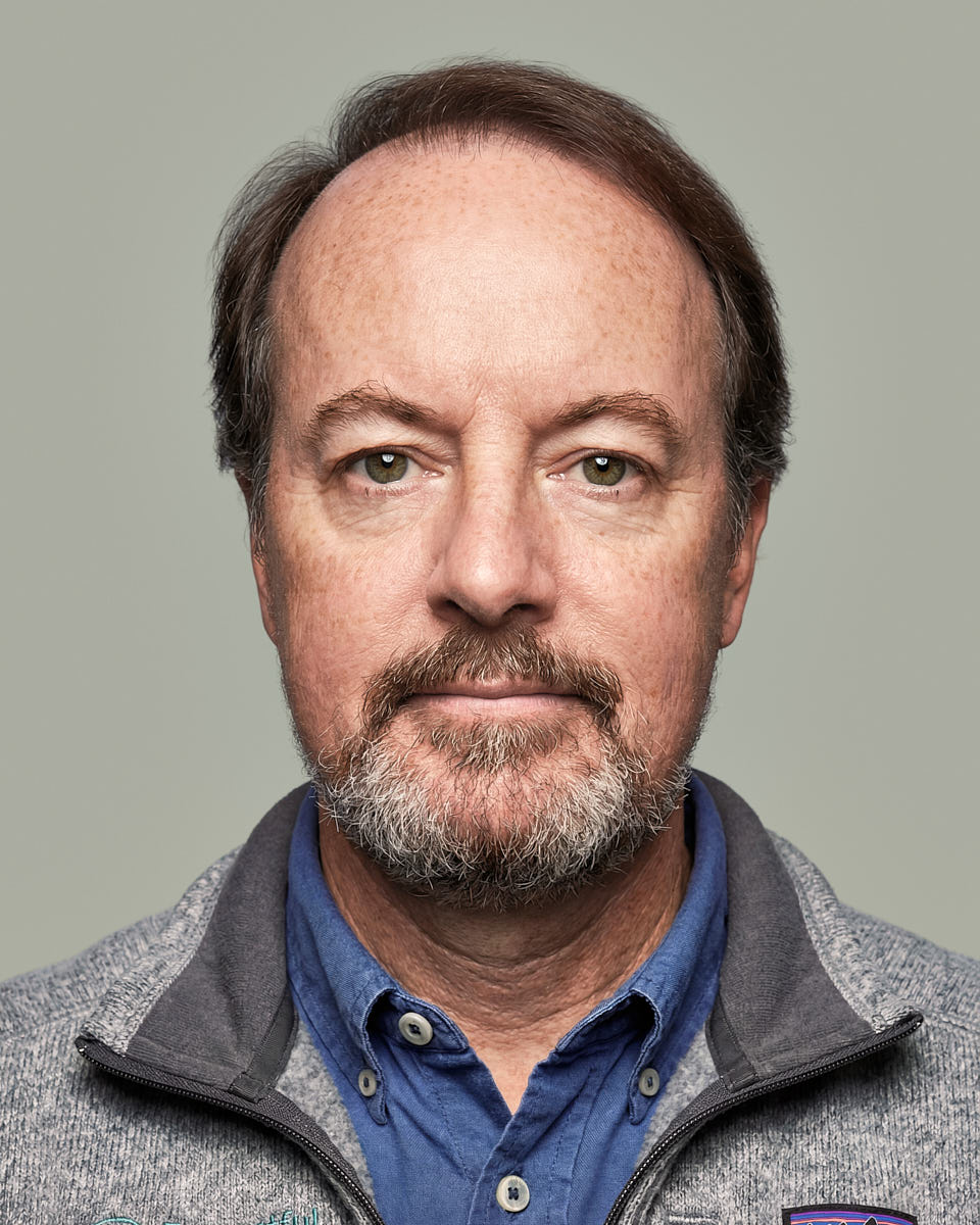 Remote headshot of a man in a gray sweater photographed against a muted neutral background.