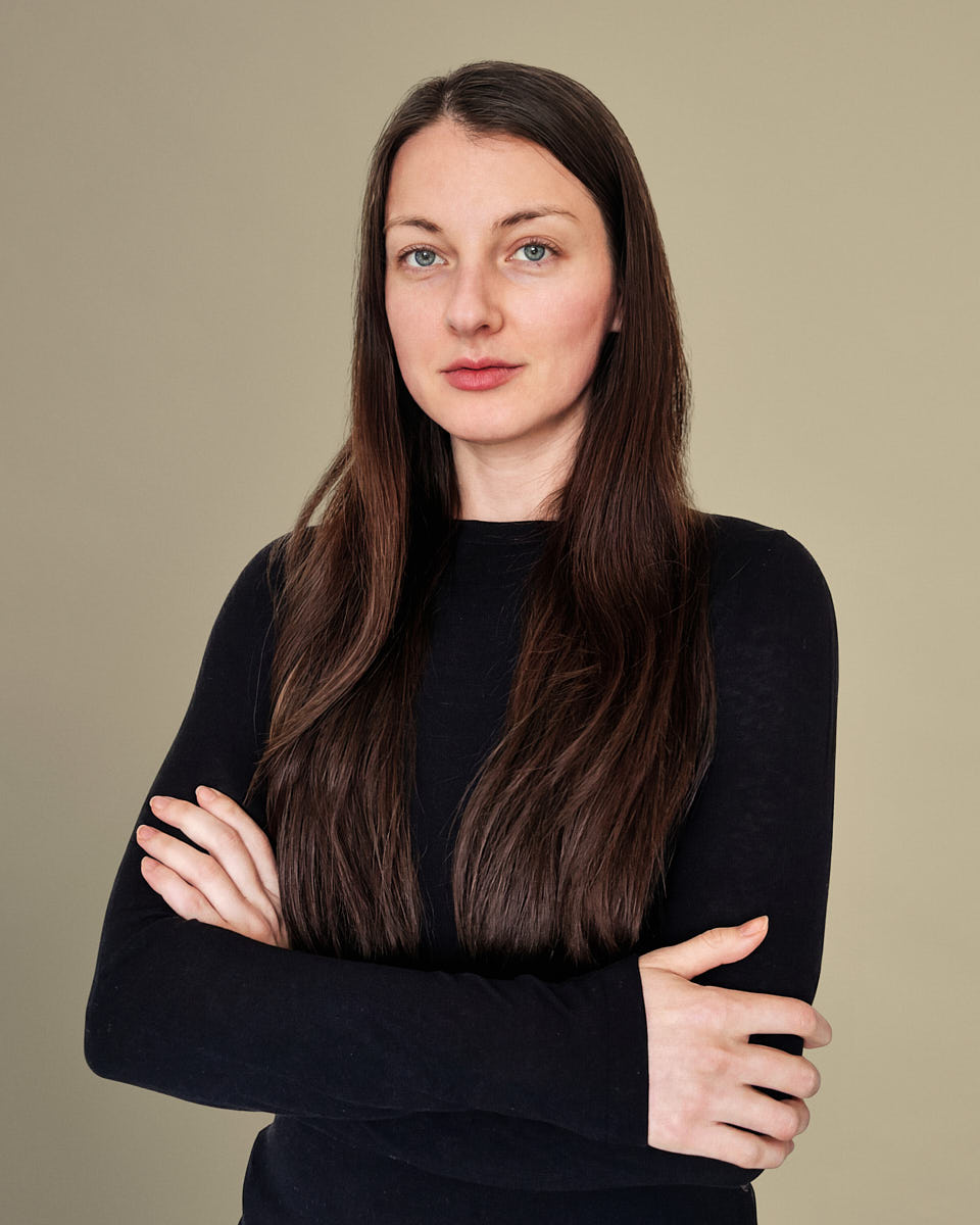 Remote headshot of a woman in a black turtleneck photographed against a warm neutral backdrop.