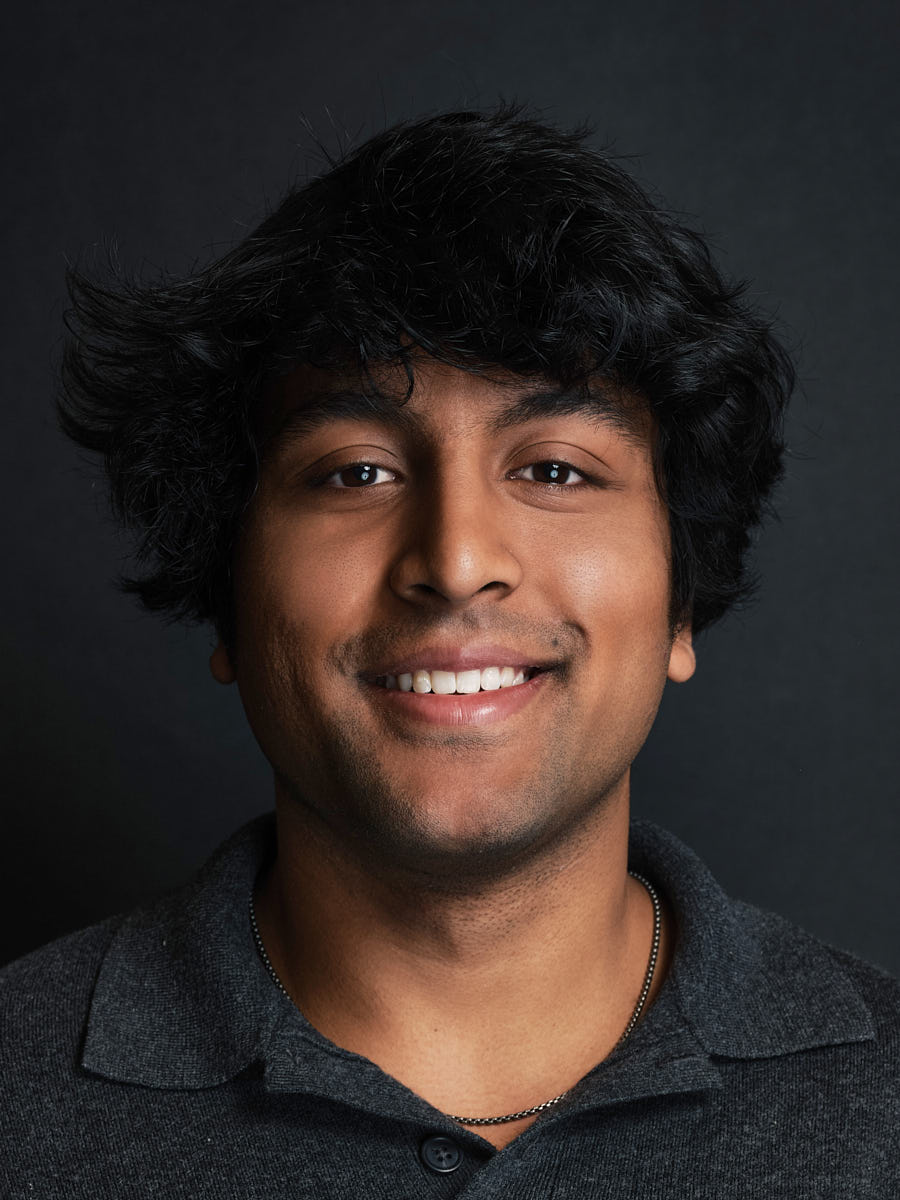 Studio headshot of a smiling young man photographed against a dark background.
