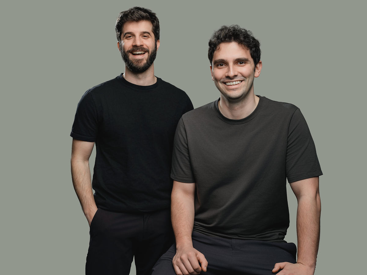 Studio team portrait of two men photographed together against a muted green background.
